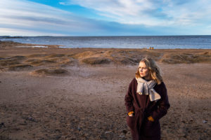 Hanna Parhaniemi seisoo hiekkarannalla, takki päällä, hieman sivusta kuvattuna.