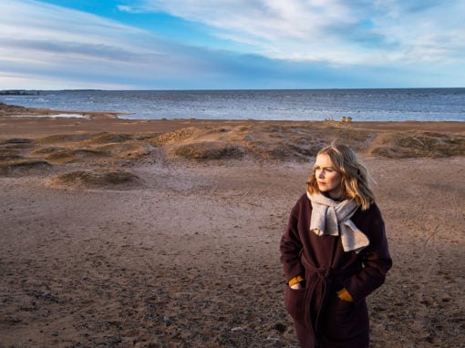 Hanna Parhaniemi seisoo hiekkarannalla, takki päällä, hieman sivusta kuvattuna.